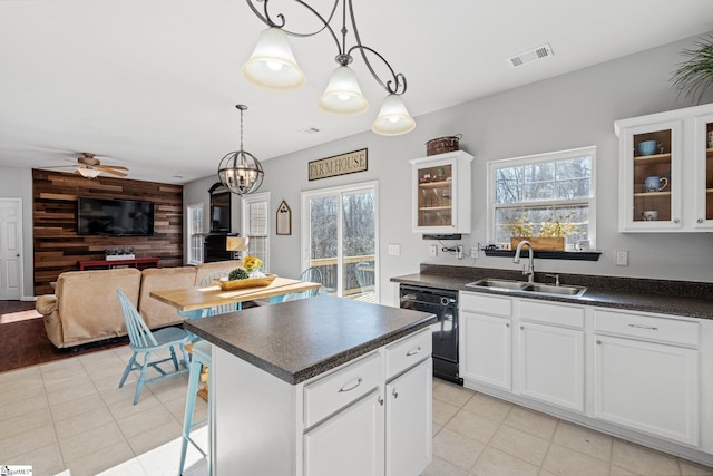 kitchen with sink, hanging light fixtures, black dishwasher, wooden walls, and white cabinets