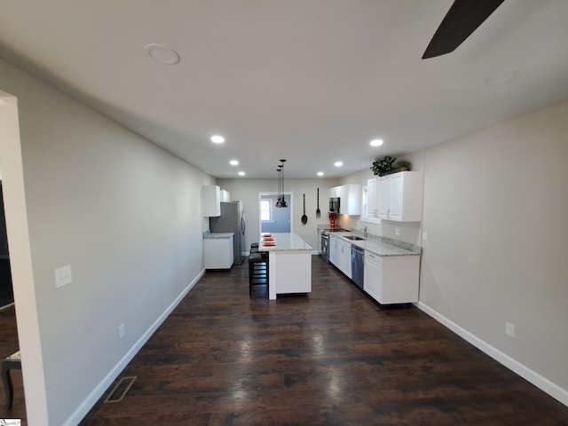 kitchen with appliances with stainless steel finishes, a center island, decorative light fixtures, white cabinetry, and a breakfast bar area