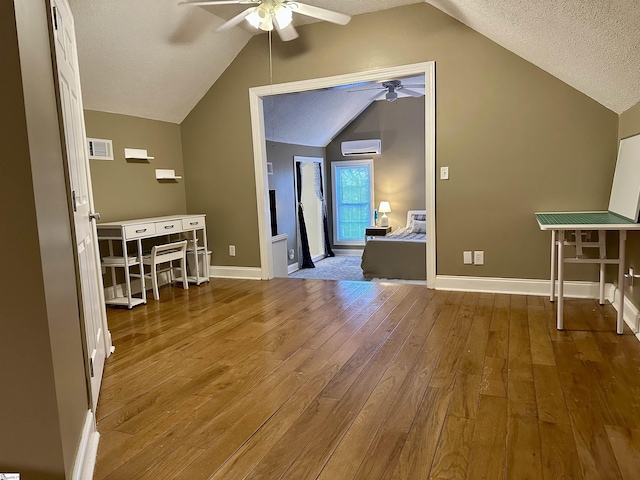 additional living space with vaulted ceiling, ceiling fan, a textured ceiling, wood-type flooring, and a wall unit AC