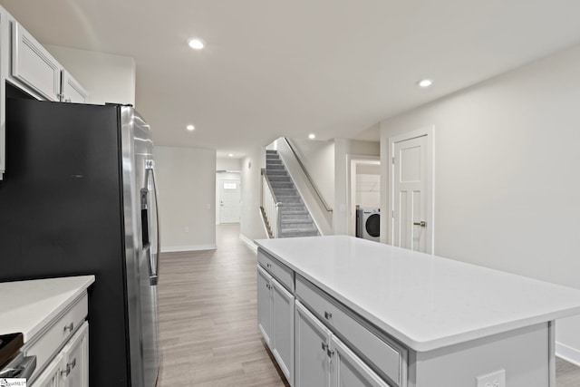 kitchen featuring washer / clothes dryer, a center island, stainless steel refrigerator with ice dispenser, and light hardwood / wood-style flooring