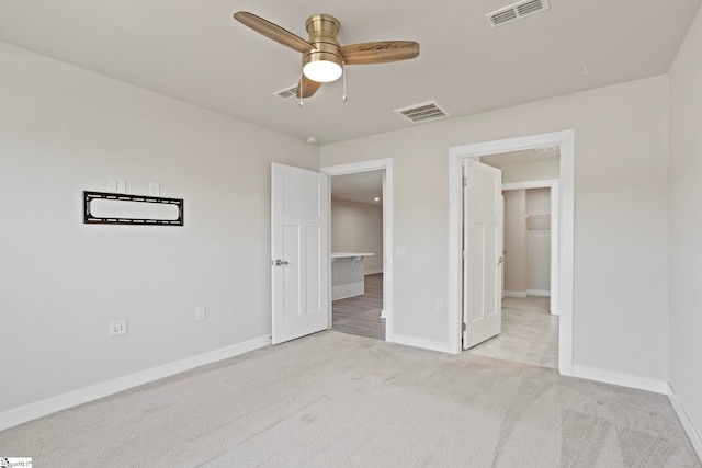 unfurnished bedroom with ceiling fan, a walk in closet, and light carpet