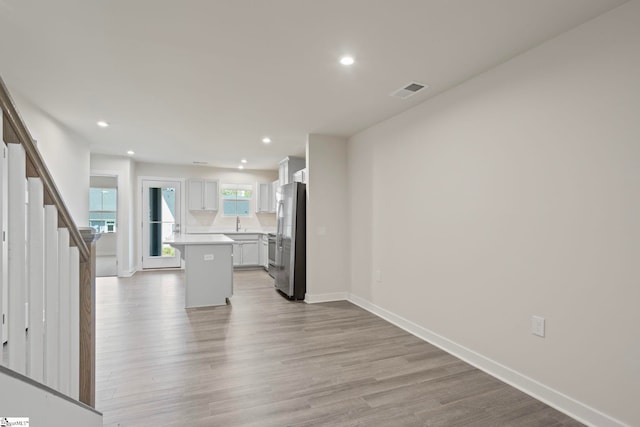 kitchen with stainless steel refrigerator, a center island, a kitchen breakfast bar, light hardwood / wood-style flooring, and white cabinets