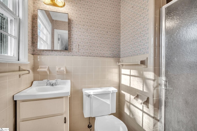 bathroom with vanity, toilet, a shower with door, and tile walls