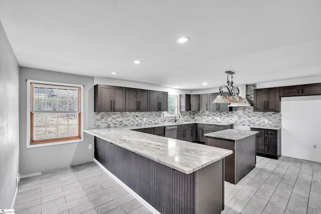 kitchen with dishwasher, wall chimney range hood, decorative light fixtures, a kitchen island, and kitchen peninsula