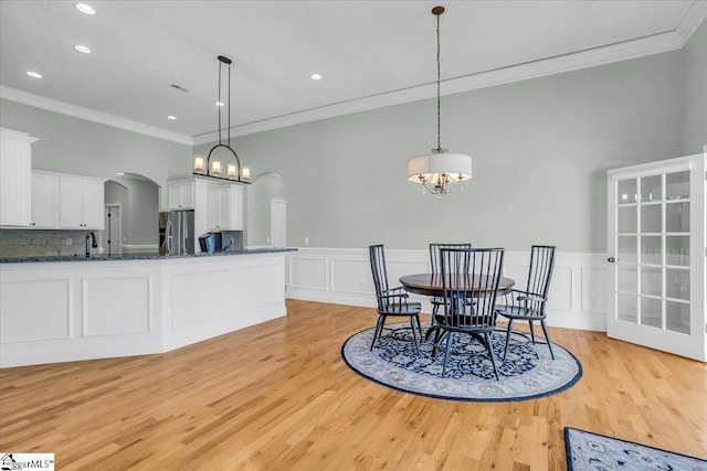 dining room with a notable chandelier, light wood-type flooring, ornamental molding, and sink