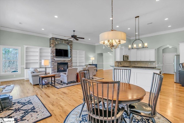 dining area with a fireplace, light hardwood / wood-style floors, ceiling fan with notable chandelier, and ornamental molding