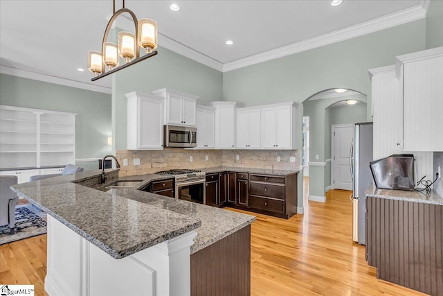 kitchen featuring kitchen peninsula, ornamental molding, stainless steel appliances, stone counters, and white cabinetry