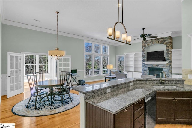 kitchen featuring dark brown cabinetry, sink, a stone fireplace, stainless steel dishwasher, and ornamental molding