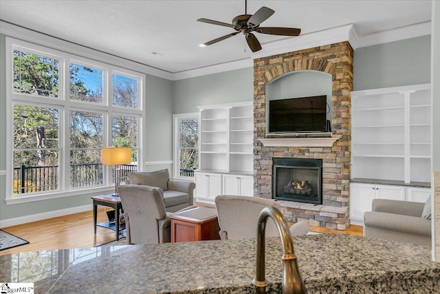 living room featuring a stone fireplace, ceiling fan, wood-type flooring, and ornamental molding