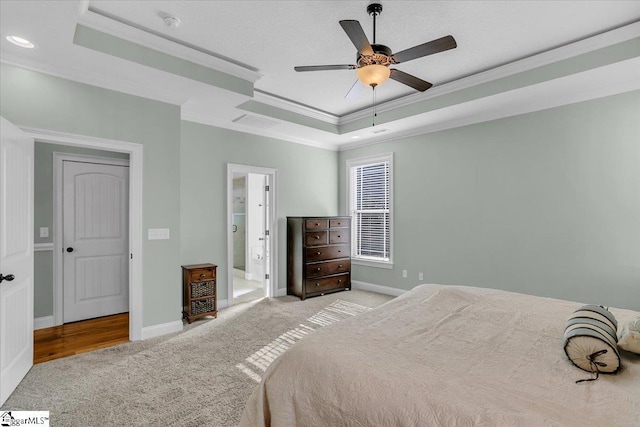 bedroom featuring ceiling fan, ornamental molding, connected bathroom, a tray ceiling, and light colored carpet