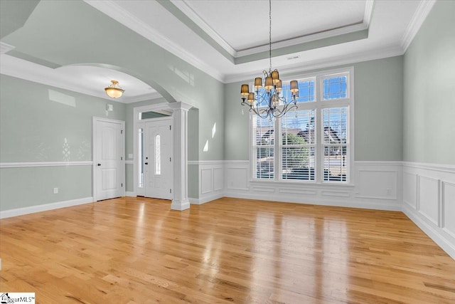 interior space featuring light wood-type flooring, ornate columns, ornamental molding, a raised ceiling, and a chandelier