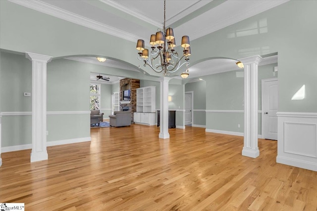 unfurnished dining area featuring ceiling fan with notable chandelier, light wood-type flooring, crown molding, and decorative columns