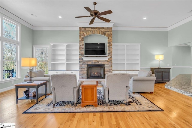 living room with a fireplace, light hardwood / wood-style flooring, ceiling fan, and ornamental molding