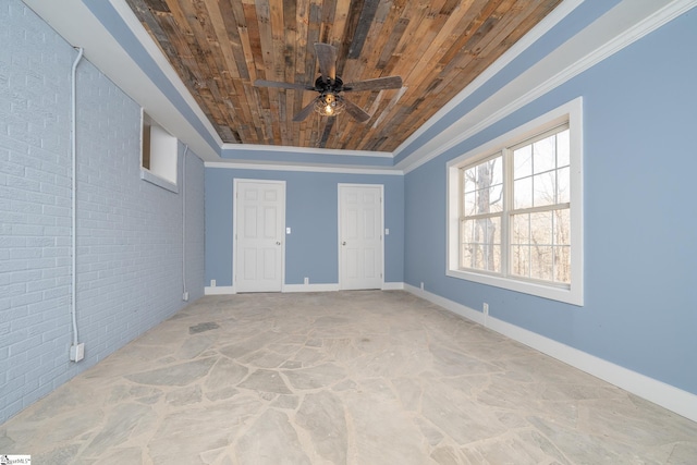 empty room featuring ceiling fan, wooden ceiling, a raised ceiling, brick wall, and ornamental molding