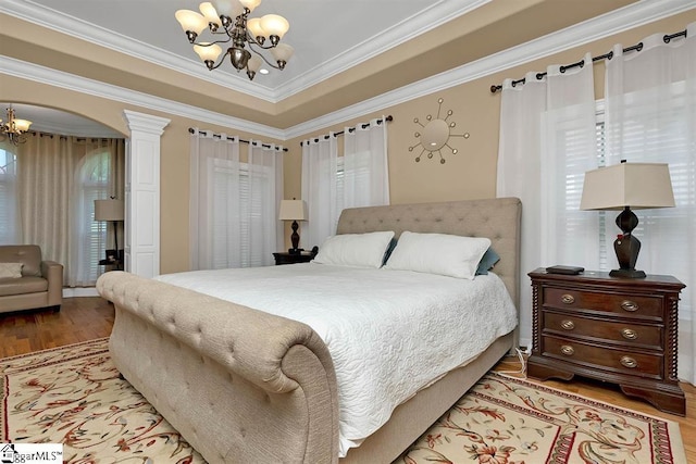 bedroom featuring light wood-type flooring, ornate columns, a tray ceiling, crown molding, and a chandelier