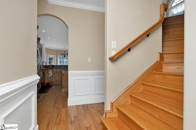 staircase with a notable chandelier, wood-type flooring, and ornamental molding