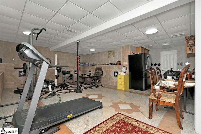 workout room with a drop ceiling, light tile patterned floors, and tile walls