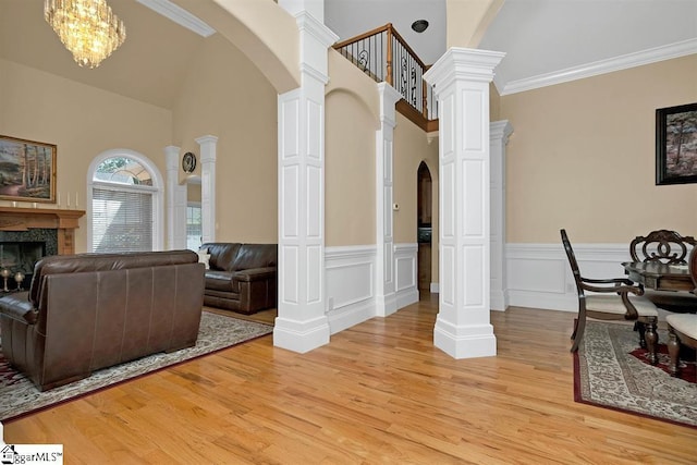 interior space featuring light wood-type flooring, ornate columns, ornamental molding, a notable chandelier, and a fireplace