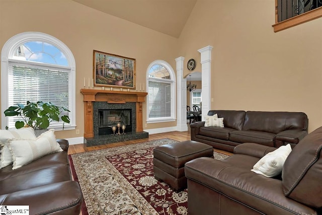 living room with a high end fireplace, wood-type flooring, high vaulted ceiling, and ornate columns