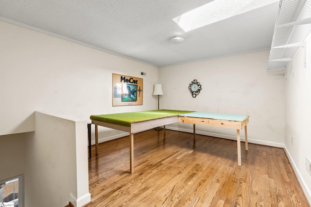 recreation room with a textured ceiling, light wood-type flooring, a skylight, and crown molding