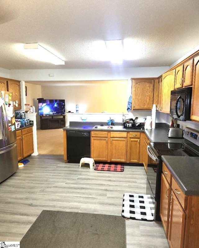 kitchen with black appliances, sink, light wood-type flooring, and a textured ceiling