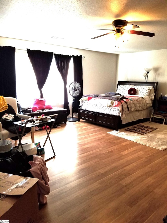 bedroom with multiple windows, ceiling fan, wood-type flooring, and a textured ceiling