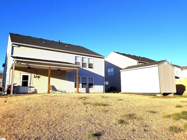 rear view of house featuring a lawn, ceiling fan, and a storage unit