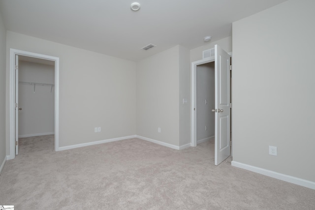 unfurnished bedroom with a walk in closet, a closet, and light colored carpet