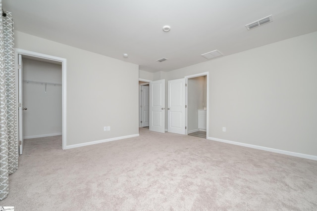 unfurnished bedroom with a walk in closet, light carpet, and ensuite bath