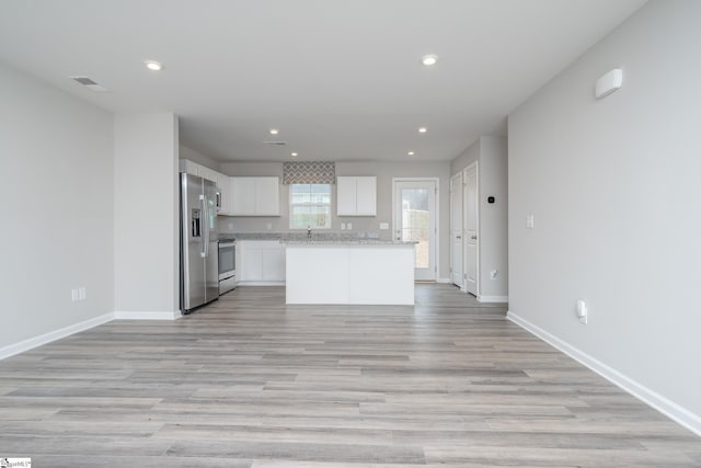 kitchen with light hardwood / wood-style flooring, a kitchen island, light stone counters, white cabinetry, and stainless steel appliances