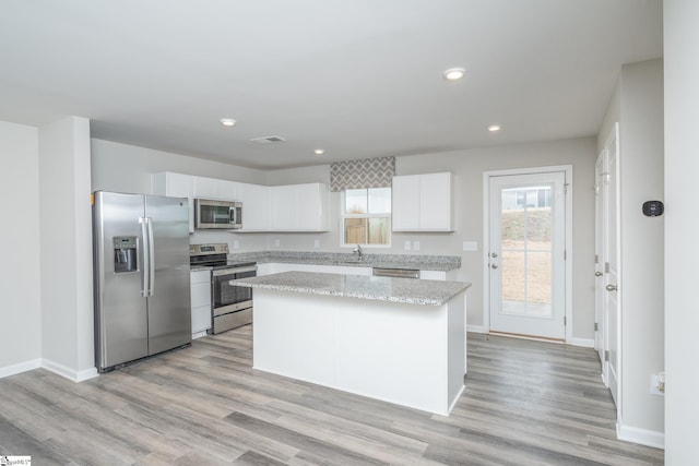 kitchen featuring light wood-type flooring, stainless steel appliances, sink, a center island, and white cabinetry