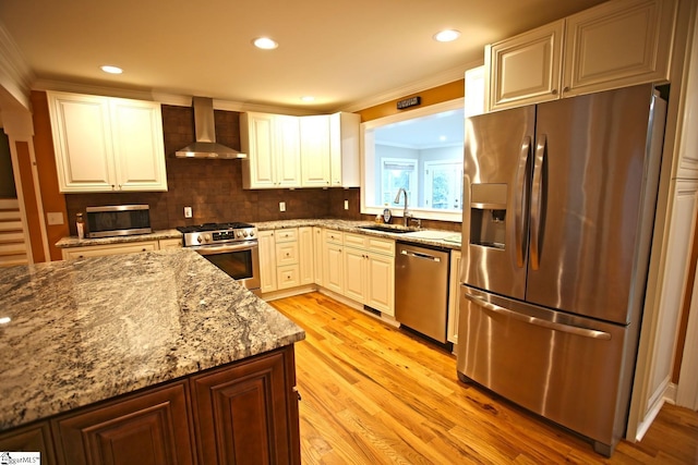 kitchen featuring light stone countertops, stainless steel appliances, sink, wall chimney range hood, and white cabinets