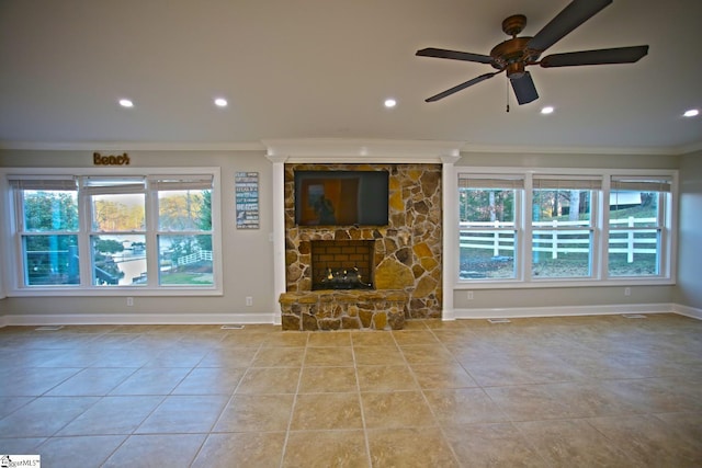 unfurnished living room featuring plenty of natural light, ceiling fan, a stone fireplace, and crown molding