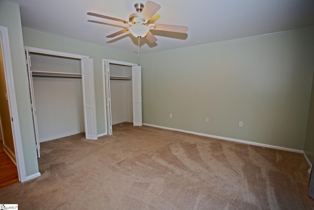 unfurnished bedroom featuring ceiling fan, light colored carpet, and two closets