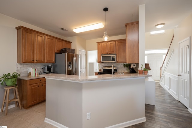 kitchen with a breakfast bar, hanging light fixtures, decorative backsplash, appliances with stainless steel finishes, and kitchen peninsula