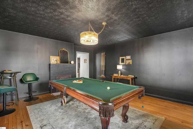 rec room featuring hardwood / wood-style floors, a chandelier, billiards, and a brick fireplace