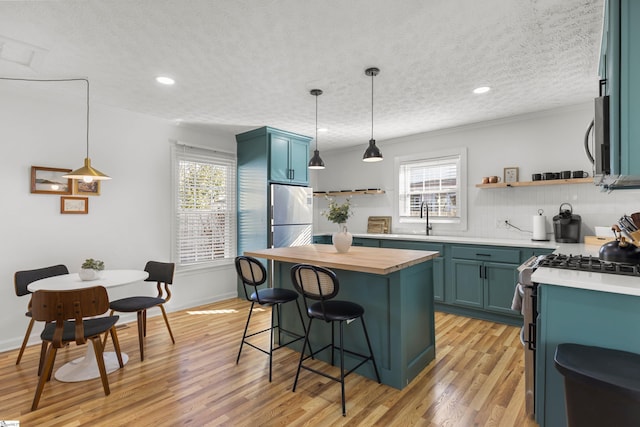 kitchen featuring appliances with stainless steel finishes, a breakfast bar, a textured ceiling, blue cabinetry, and light hardwood / wood-style flooring