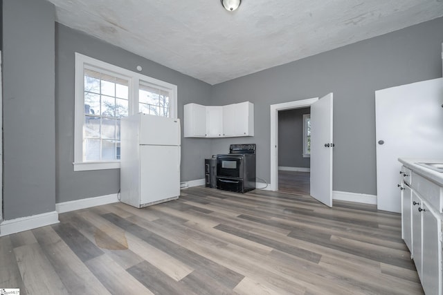 kitchen with white refrigerator, black stove, white cabinetry, and light wood-type flooring