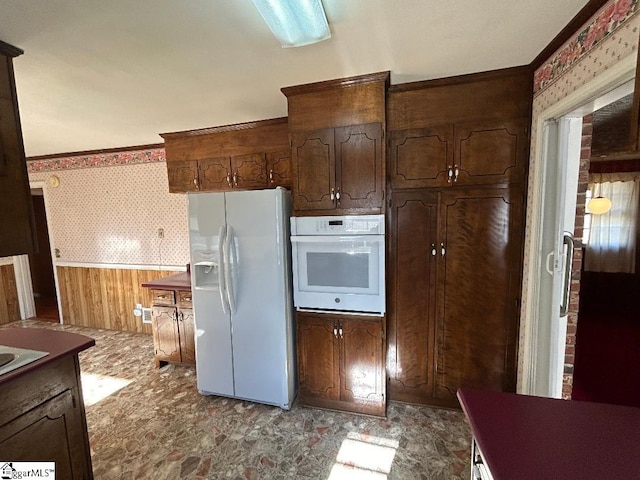 kitchen with wooden walls, dark brown cabinets, and white appliances