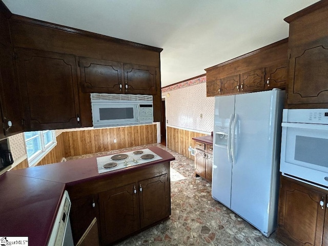 kitchen featuring dark brown cabinetry, white appliances, and wooden walls