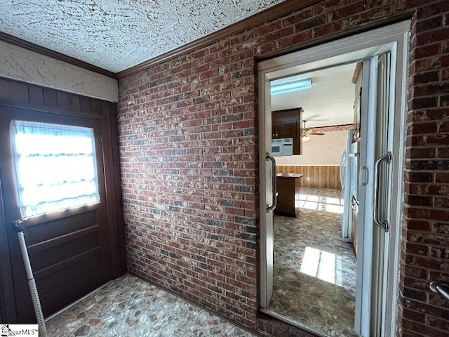 doorway to outside with a textured ceiling, wooden walls, ornamental molding, and brick wall