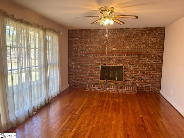 unfurnished living room featuring wood-type flooring, a brick fireplace, ceiling fan, and brick wall