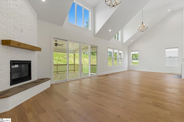 unfurnished living room featuring light hardwood / wood-style flooring, a towering ceiling, a chandelier, and a brick fireplace