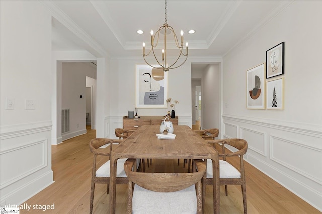 dining area featuring a raised ceiling, crown molding, light hardwood / wood-style flooring, and a chandelier