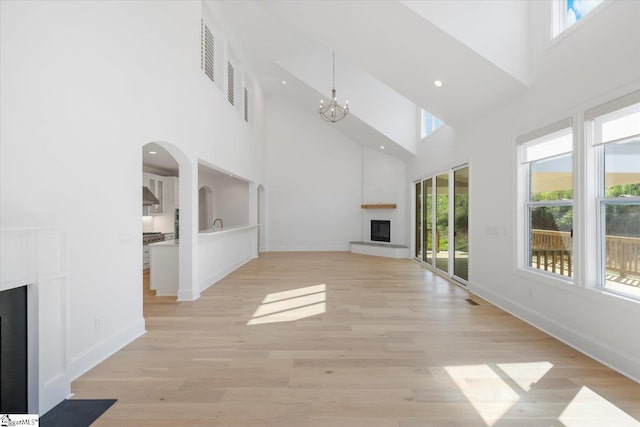 unfurnished living room with a towering ceiling, a chandelier, and a brick fireplace