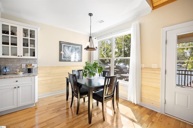 dining space with light hardwood / wood-style flooring, wooden walls, and ornamental molding