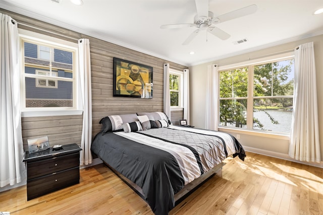 bedroom featuring ornamental molding, wood walls, ceiling fan, and light hardwood / wood-style flooring