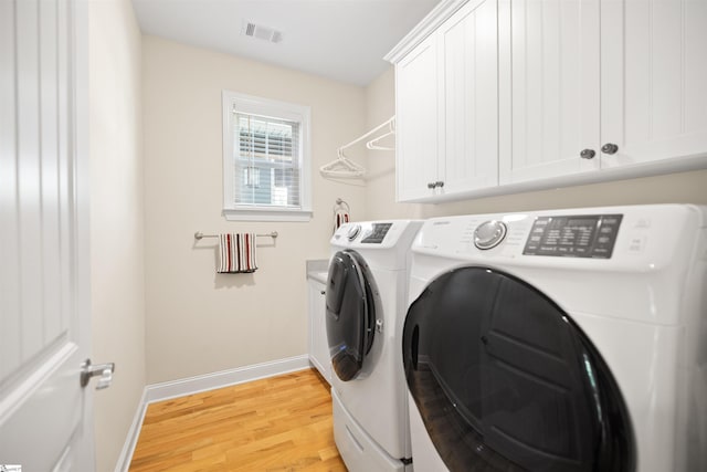 laundry room featuring light wood-type flooring, washer and dryer, and cabinets