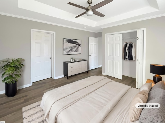 bedroom with ceiling fan, dark hardwood / wood-style floors, ornamental molding, a tray ceiling, and a closet