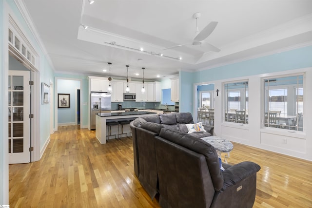 living room with ceiling fan, a raised ceiling, light wood-type flooring, and crown molding